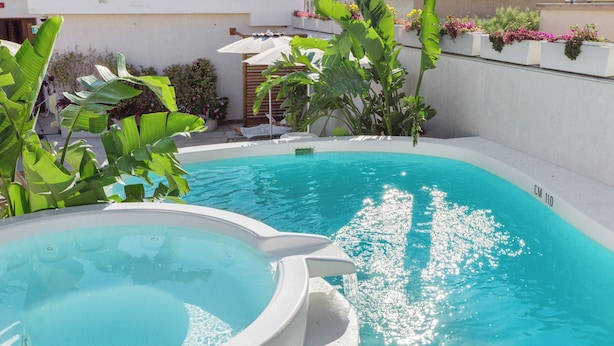 A swimming pool with a hot tub, surrounded by lush greenery and potted plants. - Hotel Domomea (Alghero)