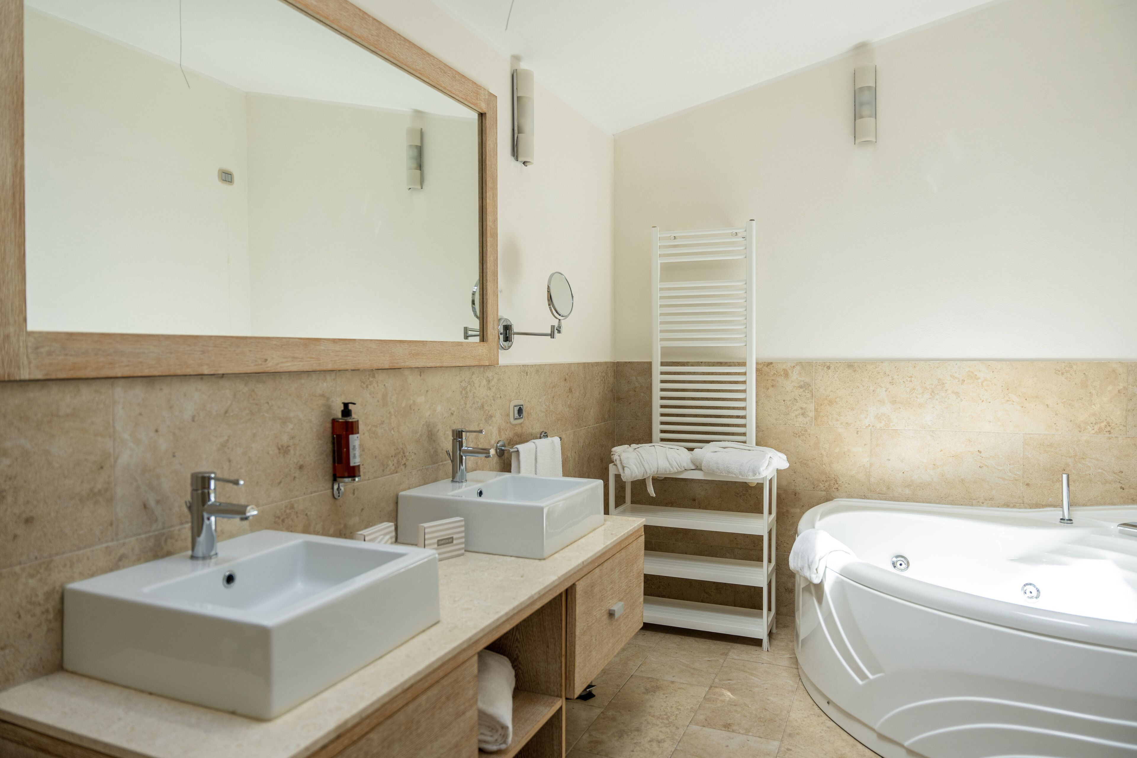 A modern bathroom with two sinks, a large mirror, a towel rack, and a bathtub.