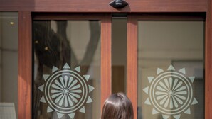 A woman standing in front of a hotel entrance with a logo and name "DOMOMEA Hotel" on the glass doors. - Hotel Domomea (Alghero)