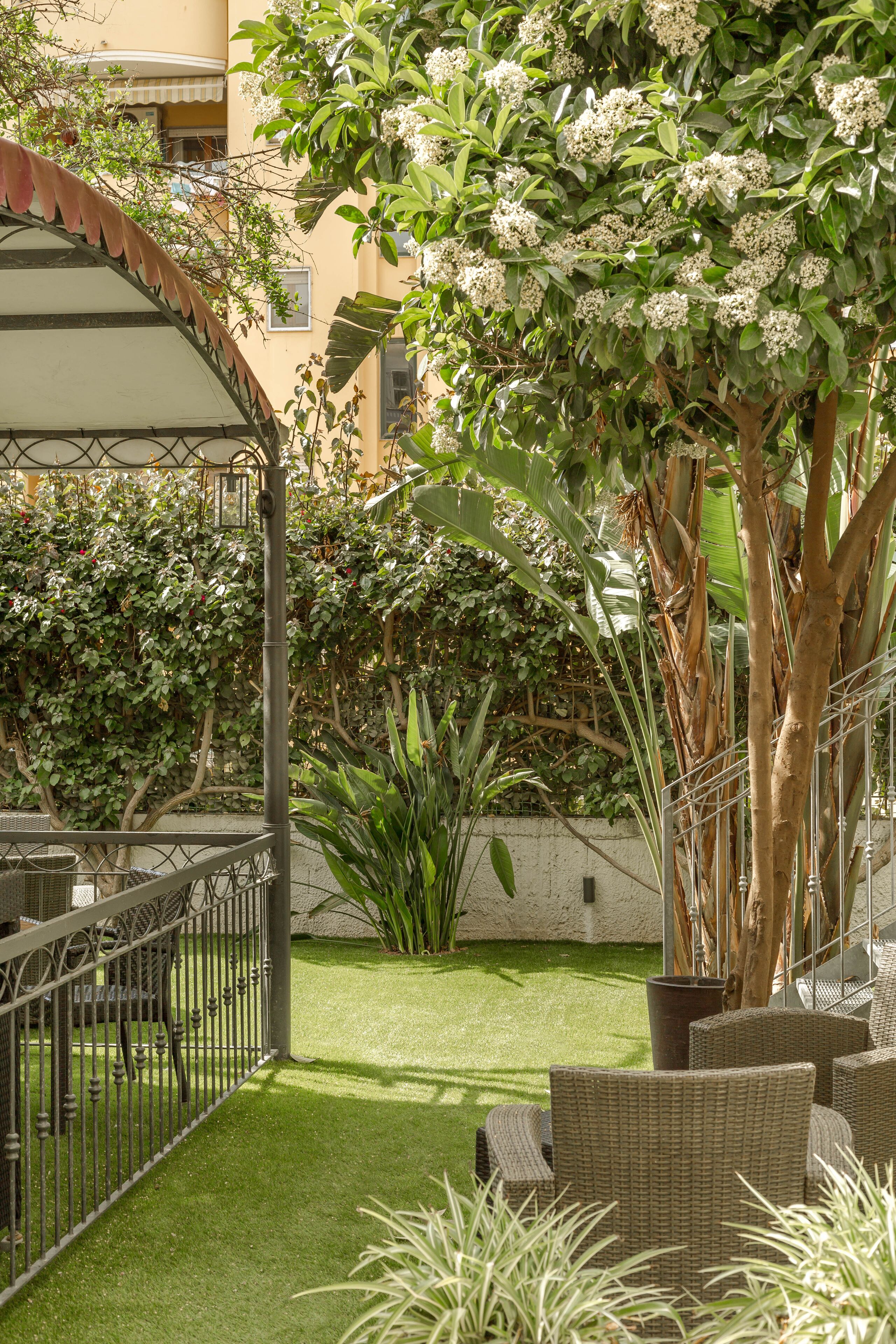 Ein Patio mit Korbmöbeln, einer überdachten Sitzgelegenheit und üppigem Grün.