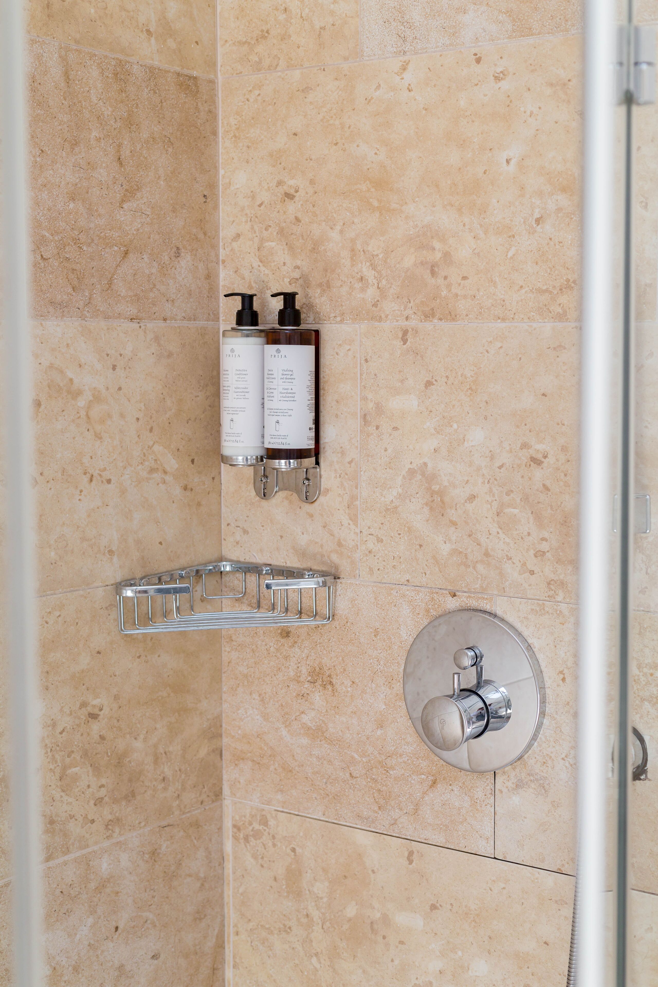 A bathroom with beige tiles, a showerhead, a soap dispenser, and a towel rack.