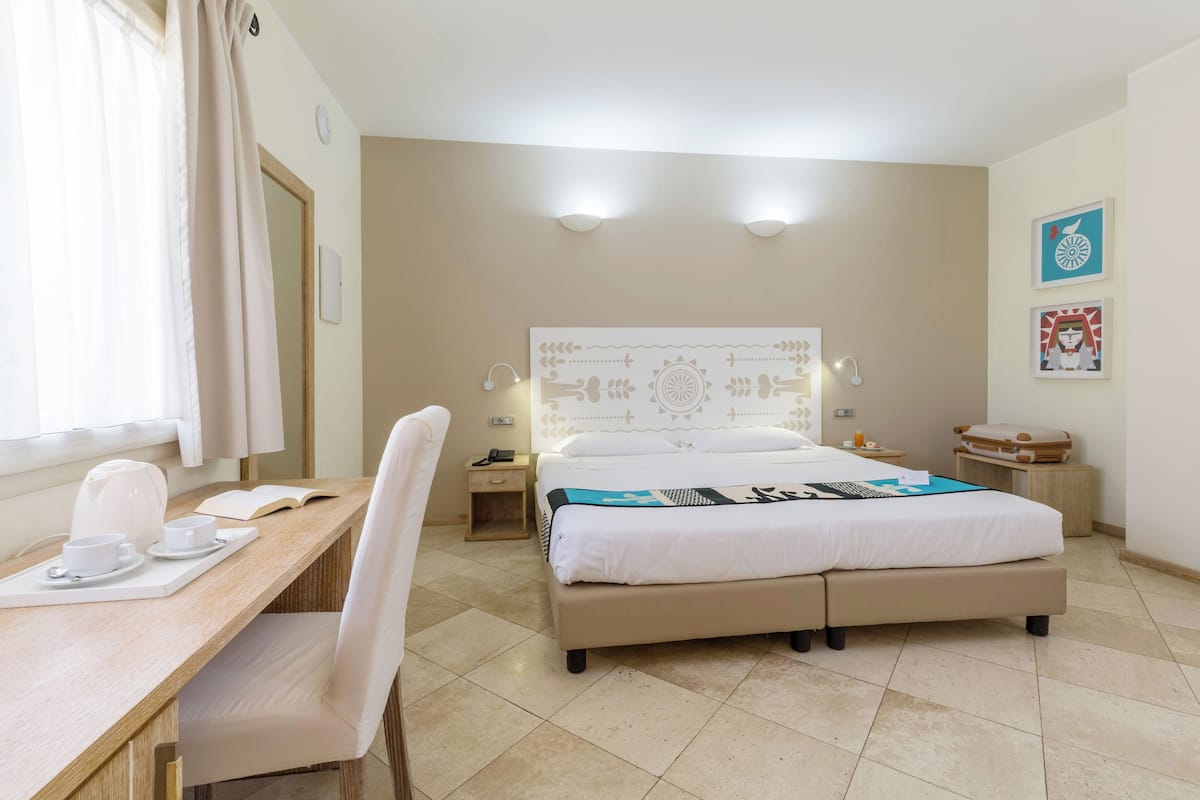 A hotel room with a bed, bedside table, chair, desk, and a window with curtains.