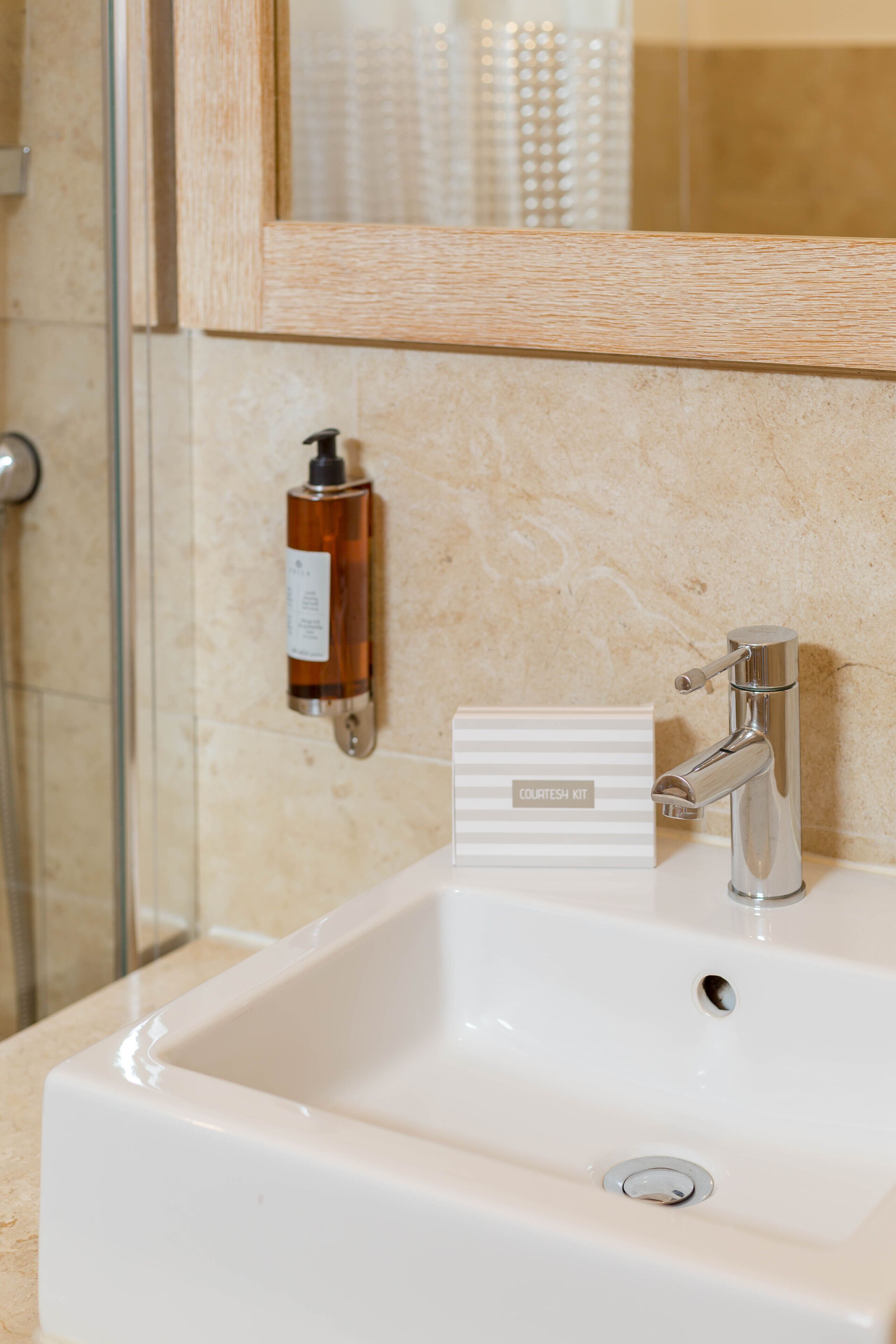 A bathroom with a white sink, a chrome faucet, a bottle of soap, and a mirror with a wooden frame.