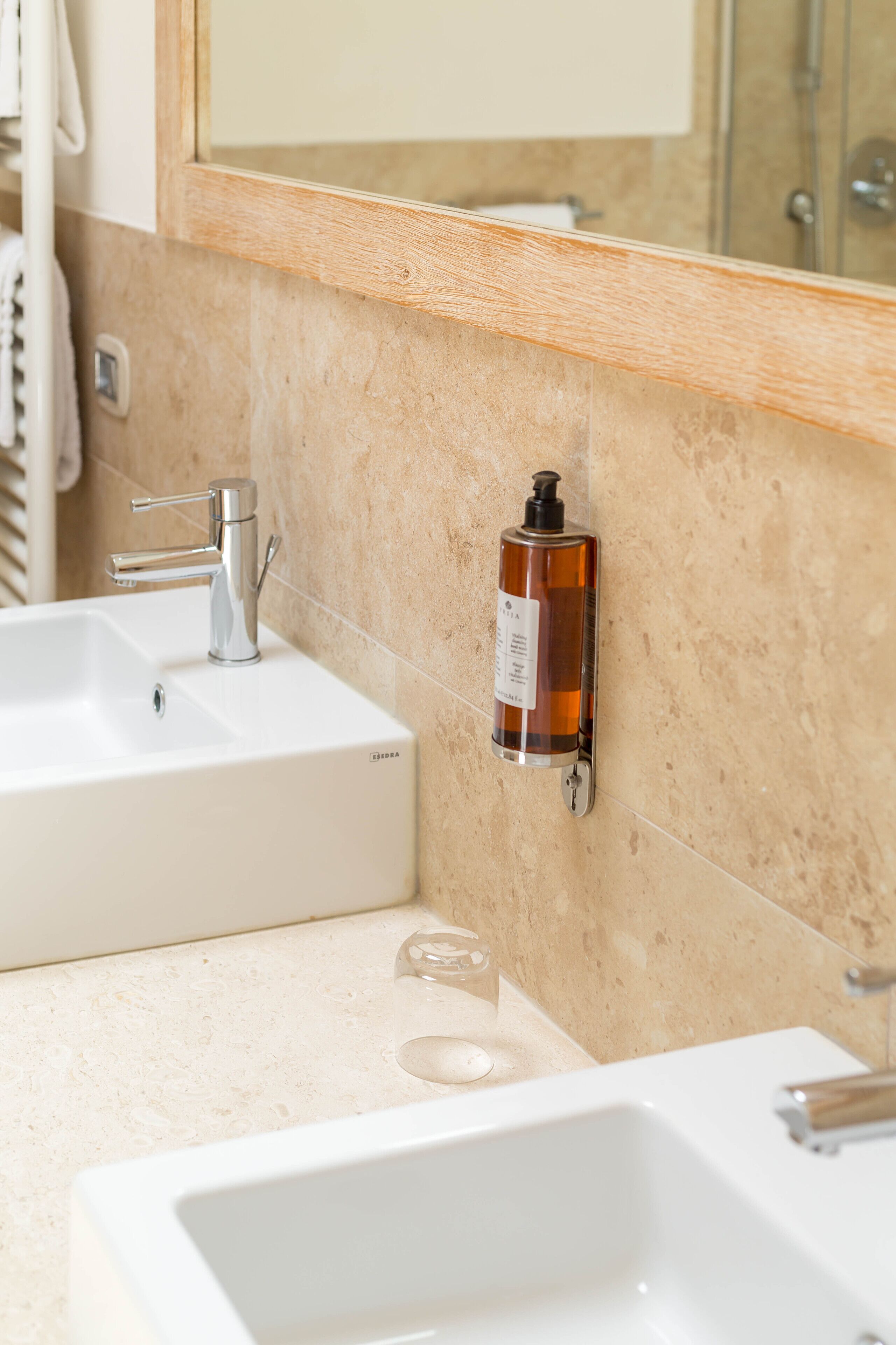 A bathroom with two sinks, a mirror, and a soap dispenser mounted on the wall.