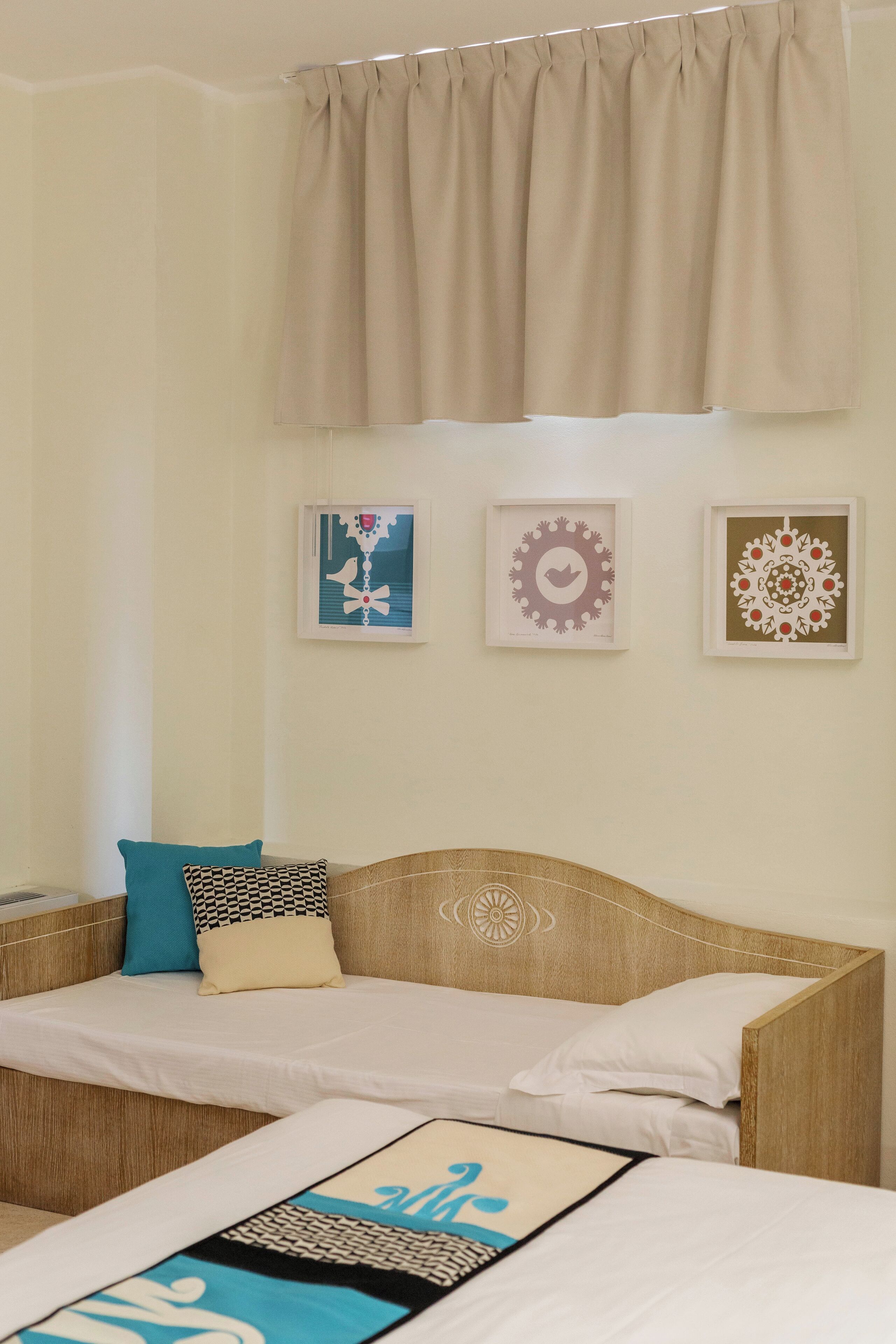 Une chambre d’hôtel avec deux lits simples, une tête de lit en bois, un rideau beige et trois œuvres d’art encadrées accrochées au mur.