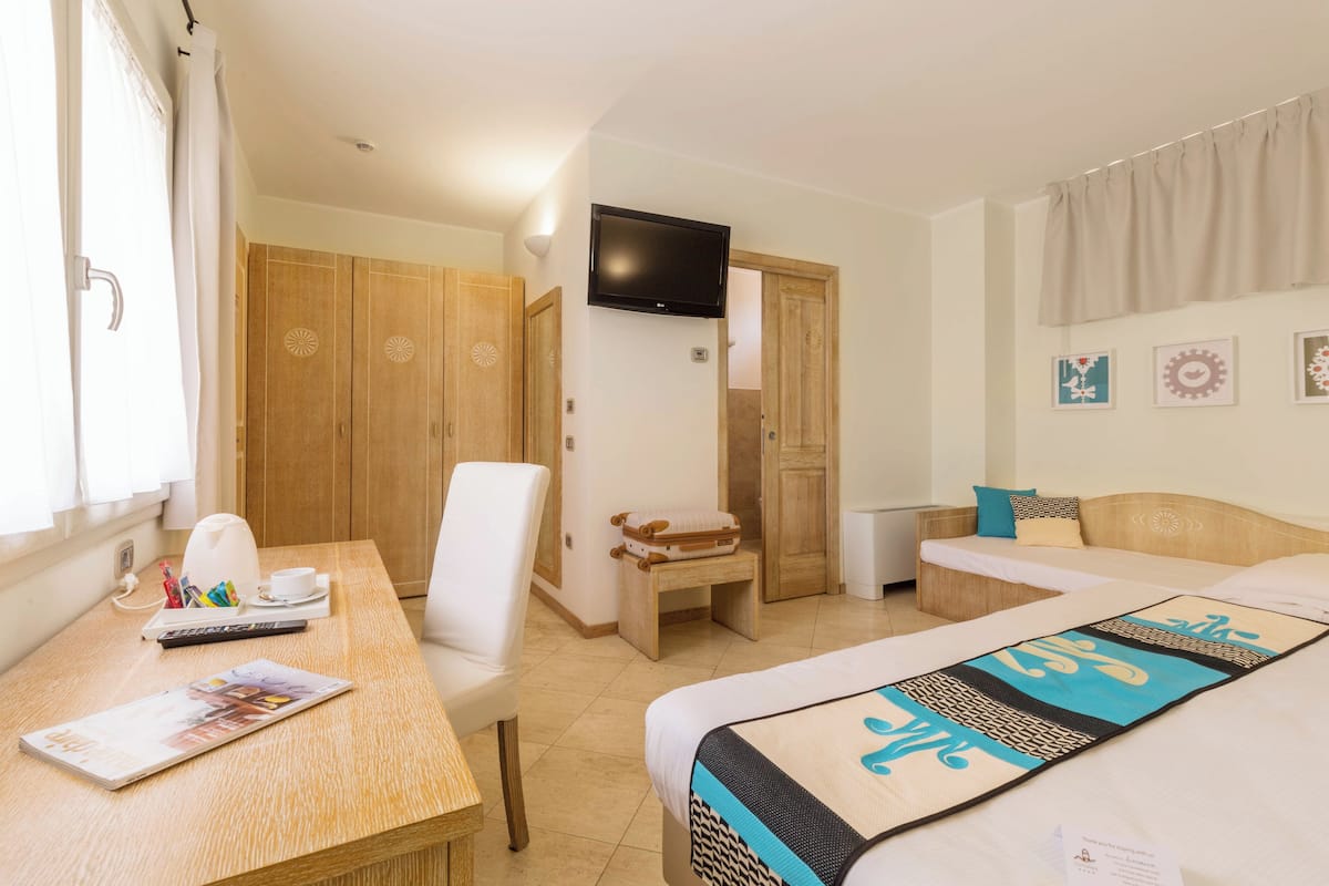 A hotel room with a bed, a desk with a chair, a television, and a wardrobe.