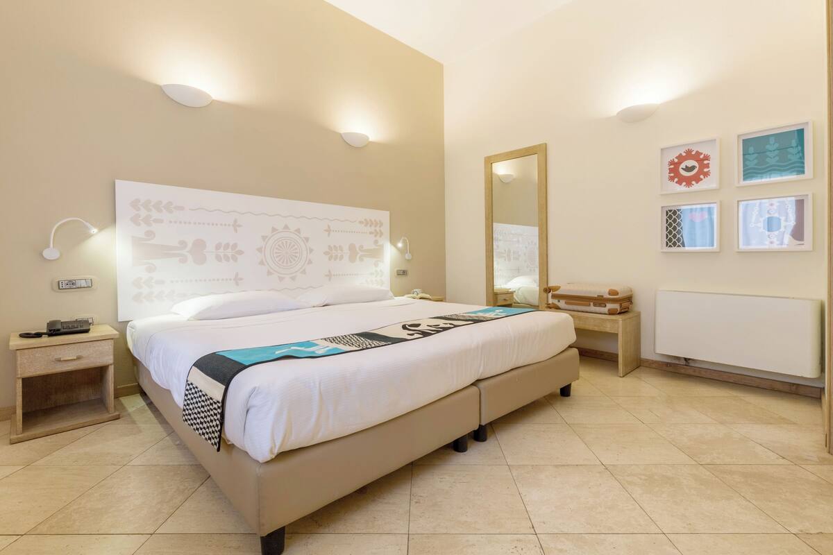 A hotel room with a large bed, bedside tables, a mirror, and wall art.