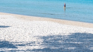 A beach with clear turquoise water, a sandy shore, and a distant lighthouse. - Hotel Domomea (Alghero)