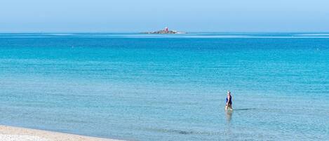 Una playa con aguas turquesas cristalinas, una orilla arenosa y un faro distante.