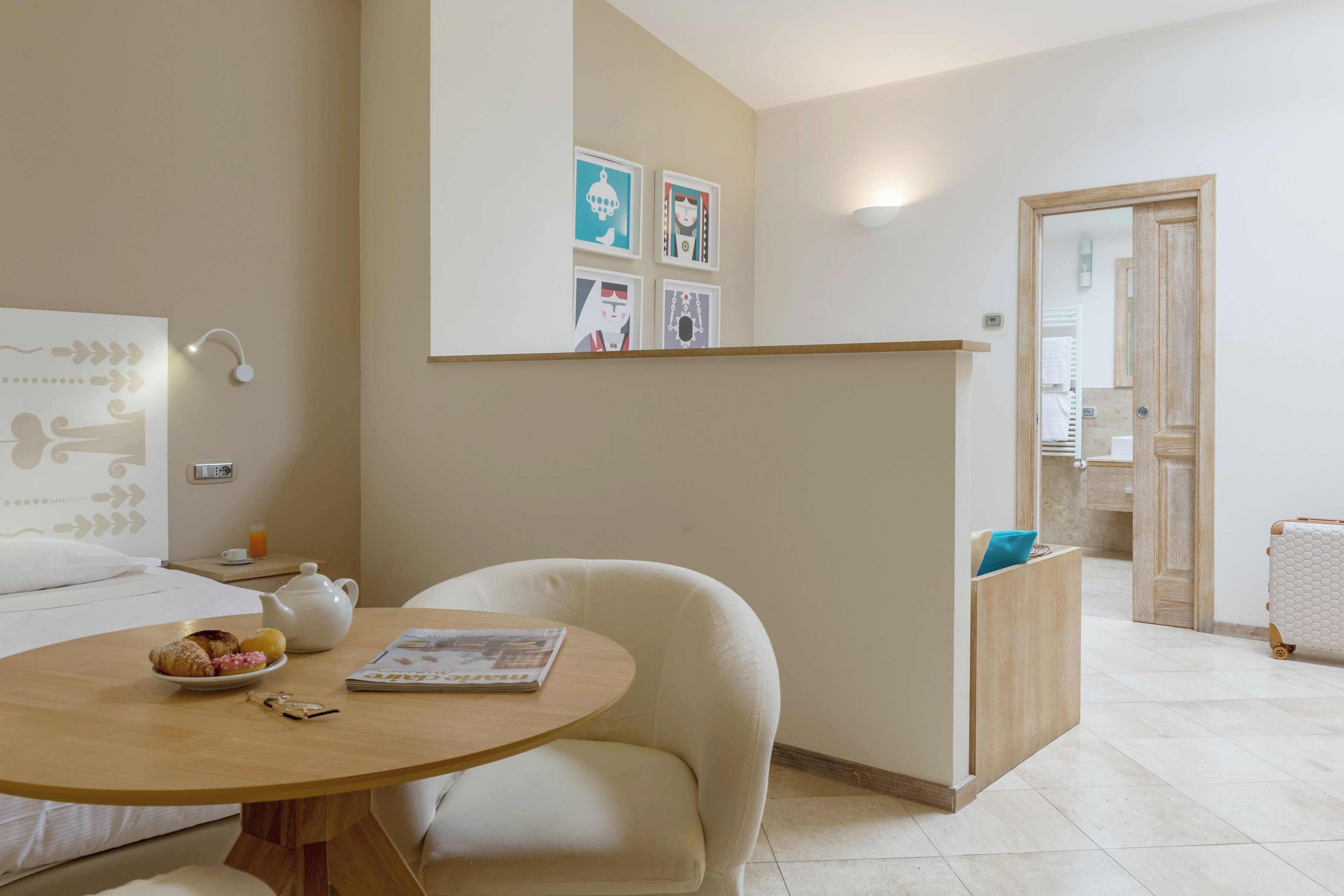 A hotel room with a bed, a round table with breakfast, a chair, a small cabinet, and a door leading to a bathroom.