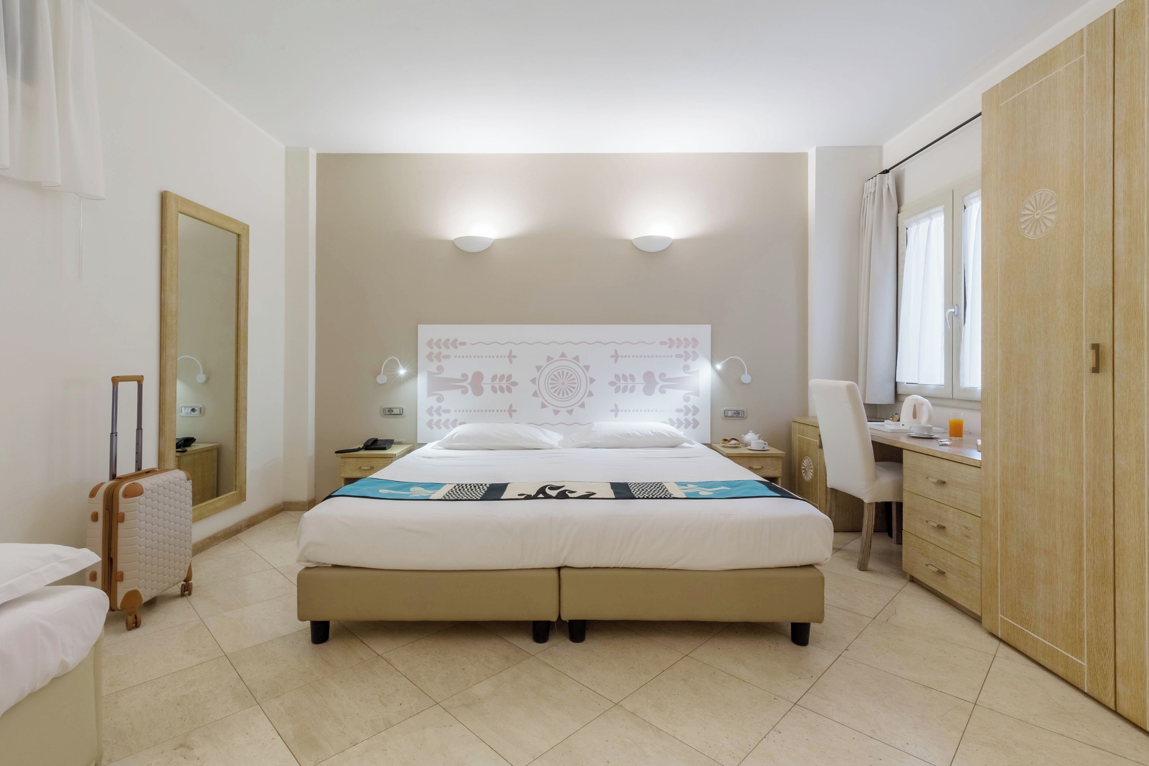 A hotel room with a large bed, a desk, a chair, a wardrobe, and a mirror.