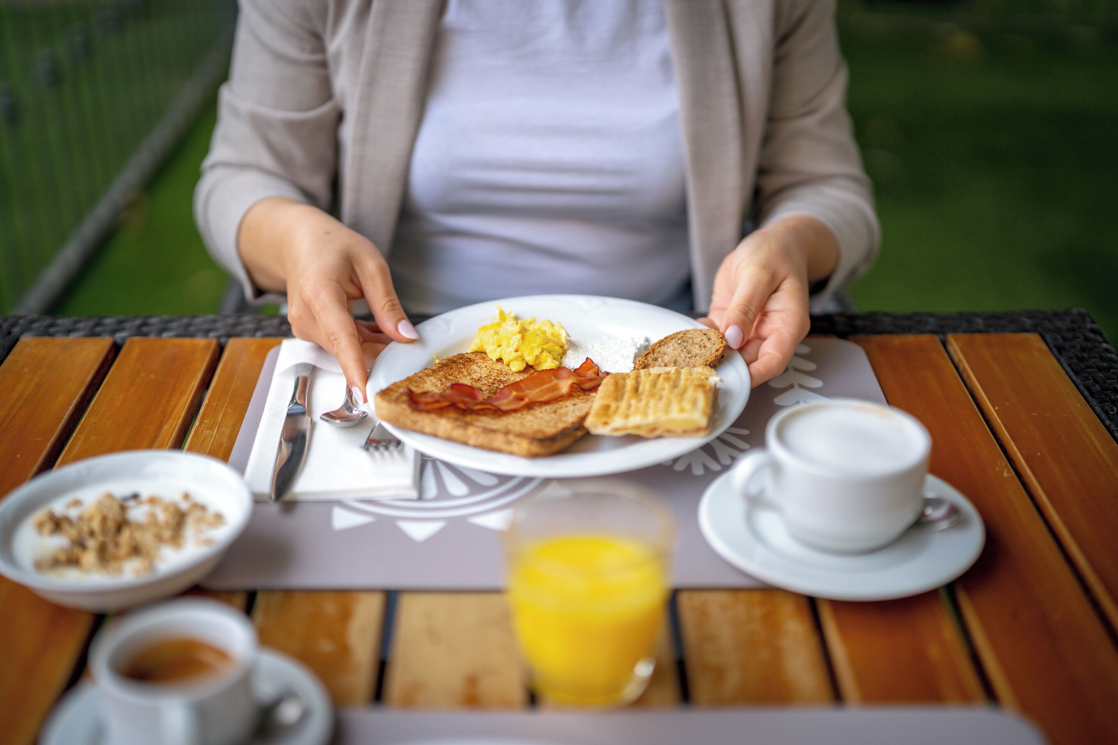 Bandeja de desayuno con tostadas, huevos revueltos y tocino sobre una mesa de madera.