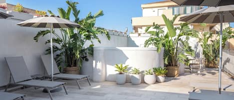 Un patio en la azotea con sillones, sombrillas y plantas en macetas.