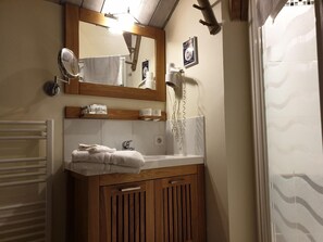 Un baño con tocador de madera, un espejo, toallero, secador de pelo y cortina de ducha.