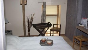 Un dormitorio con cama, una mesita con dos cuencos, una silla, un banco de madera, una ventana con persianas y un tragaluz.