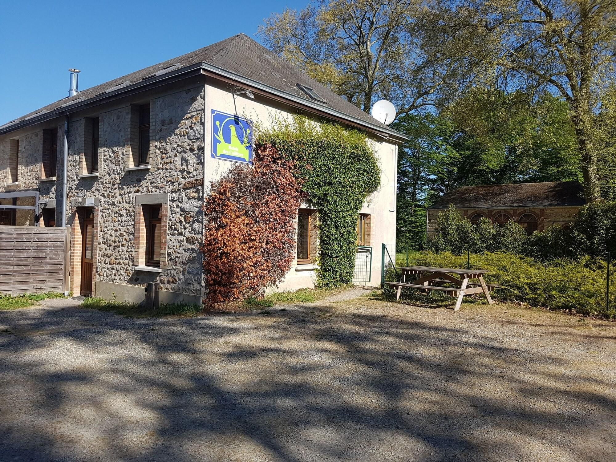 Un bâtiment en pierre avec une enseigne bleue, une clôture en bois et une allée gravillonnée.