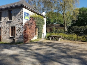A stone building with a flag, a picnic table, and a gravel driveway. - Relais des Caillères (Saint-Pavace)