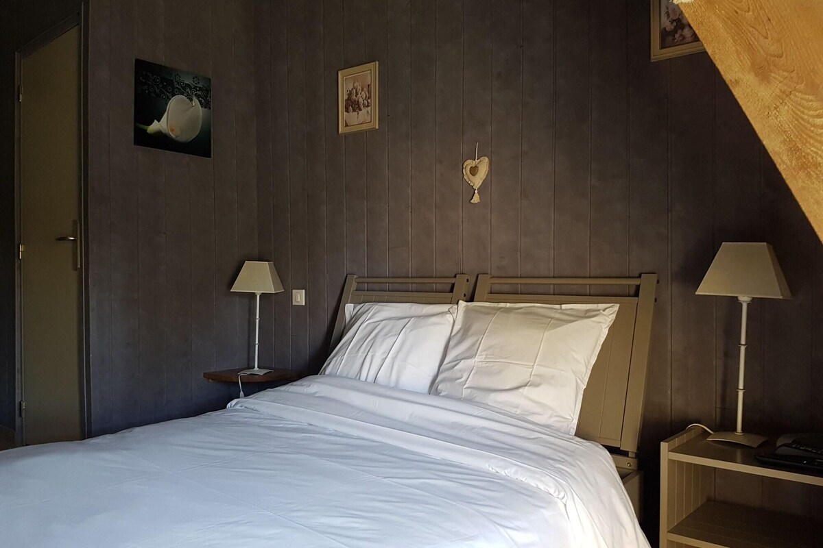 Una camera da letto con una testiera in legno, due comodini con lampade, un letto con biancheria da letto bianca e opere d'arte appese al muro.