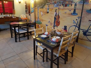 A dining area with a table set for two, chairs, and a mural on the wall. - Relais des Caillères (Saint-Pavace)