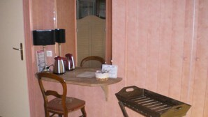 Una habitación pequeña con una mesa de madera, dos sillas, una mesita con una bandeja y un altavoz en la pared.