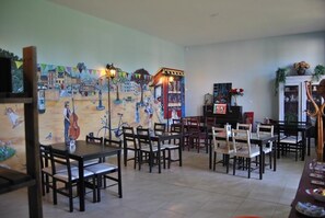 A dining area with tables and chairs, a mural on the wall, and a piano in the background. - Relais des Caillères (Saint-Pavace)