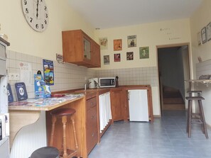 Una cocina compacta con armarios de madera, un refrigerador blanco, un microondas y un reloj en la pared.