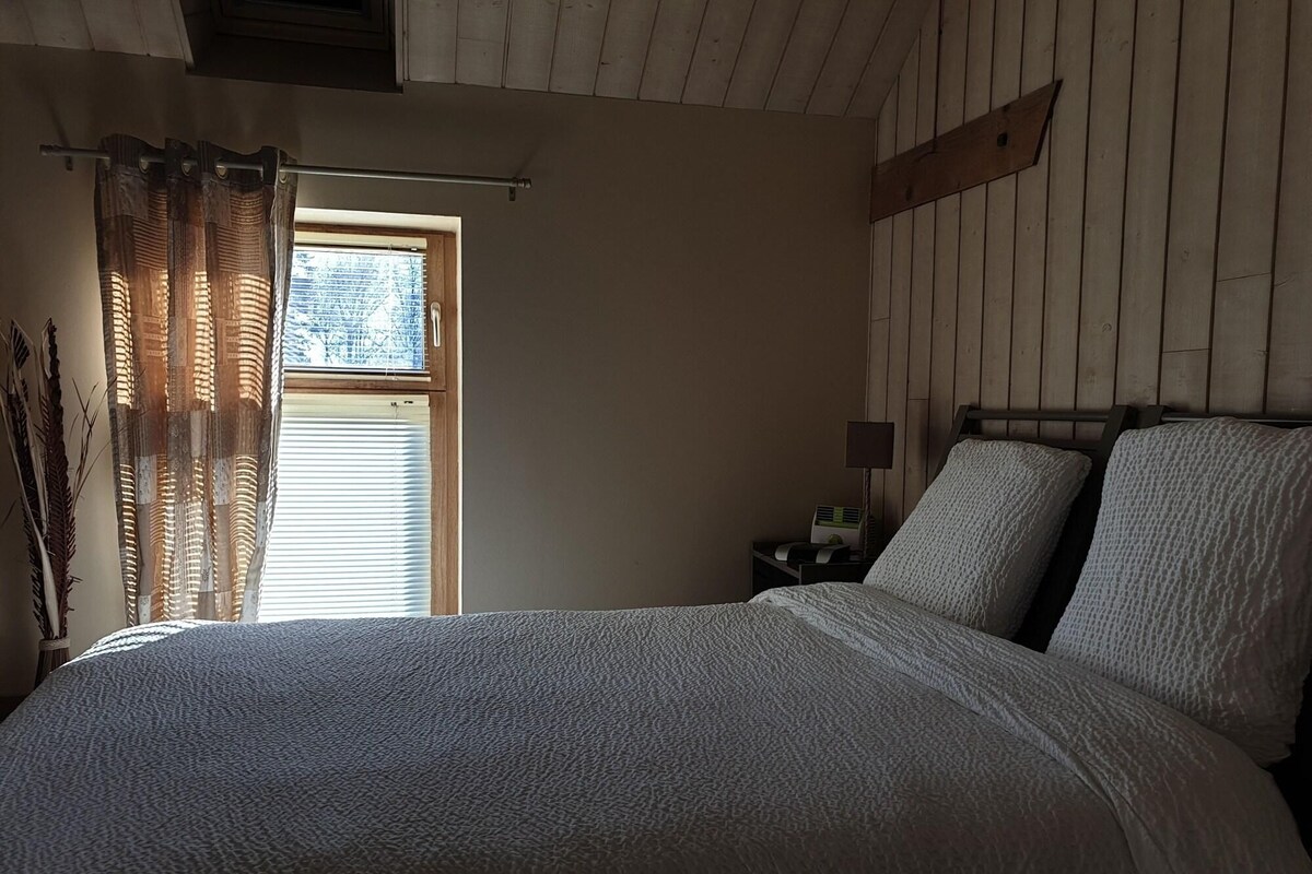 Una camera da letto con un letto grande, pareti in legno, una finestra con tende e un comodino con una lampada.