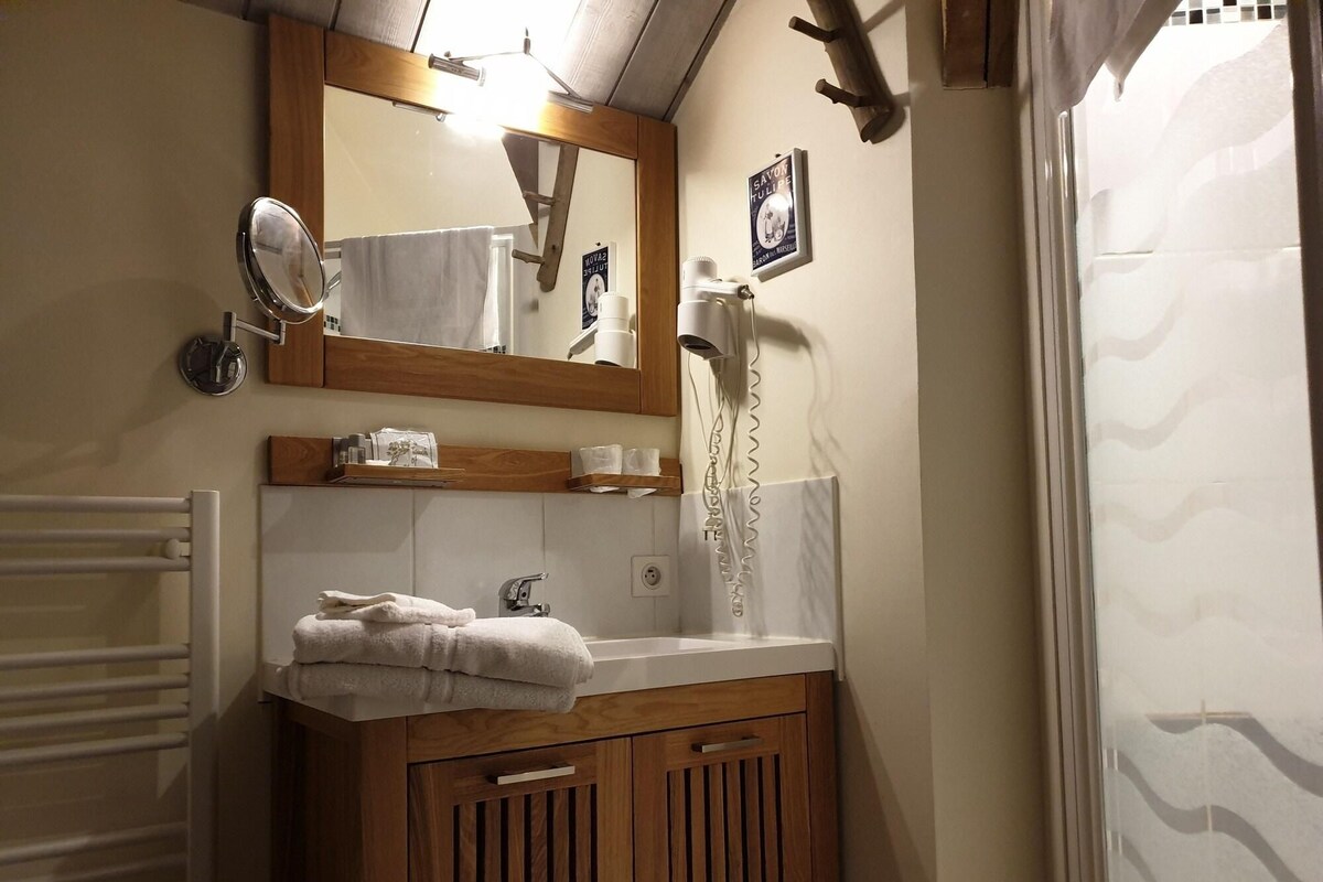 Un bagno con un mobile contenitore in legno, uno specchio, un portasciugamani, un asciugacapelli e una tenda da doccia.