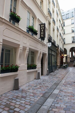 Un hôtel avec une enseigne, des plantes en pot et une rue pavée.