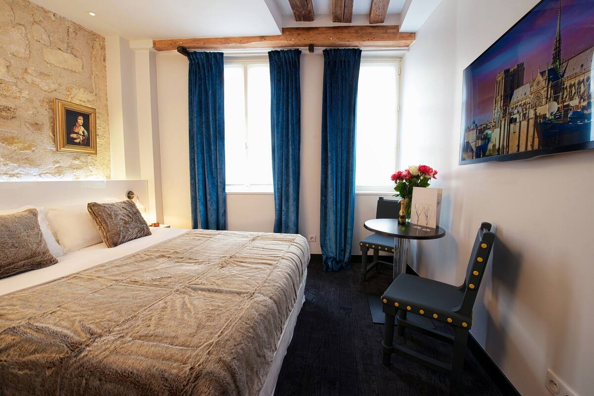 Una habitación de hotel con una cama, una mesa con flores, una silla y un cuadro en la pared.