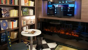 Una biblioteca con estanterías, televisor, chimenea y un sillón.