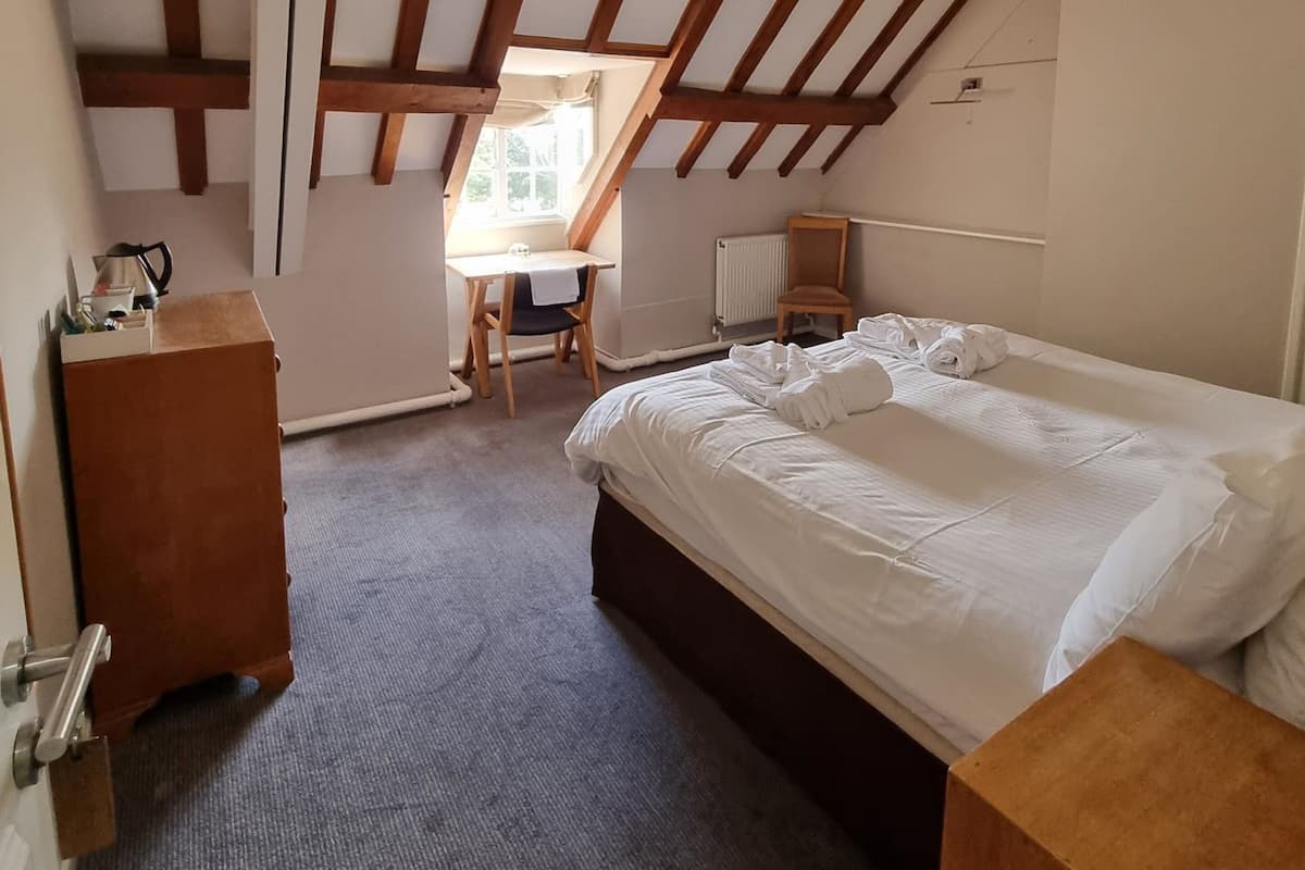 A bedroom with a large bed, a desk, and a chair. There is a window providing natural light.