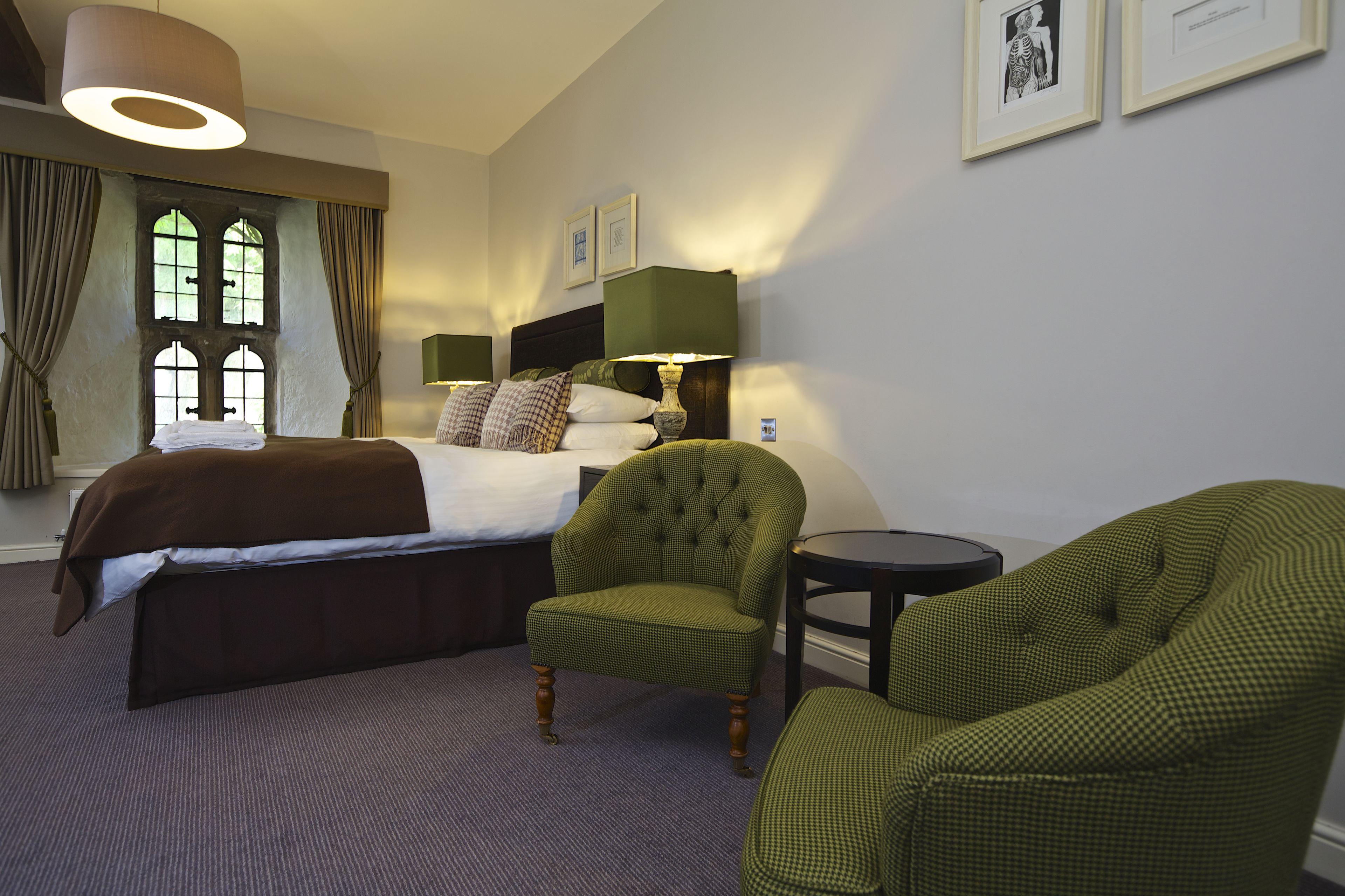 Een hotelkamer met een bed, twee fauteuils, een tafeltje en een raam met gordijnen.