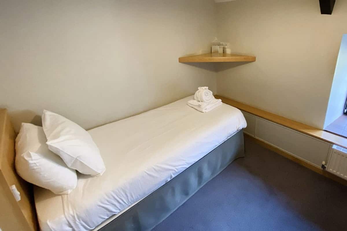 A single bed with white linens, a wooden headboard, and a small shelf above it.