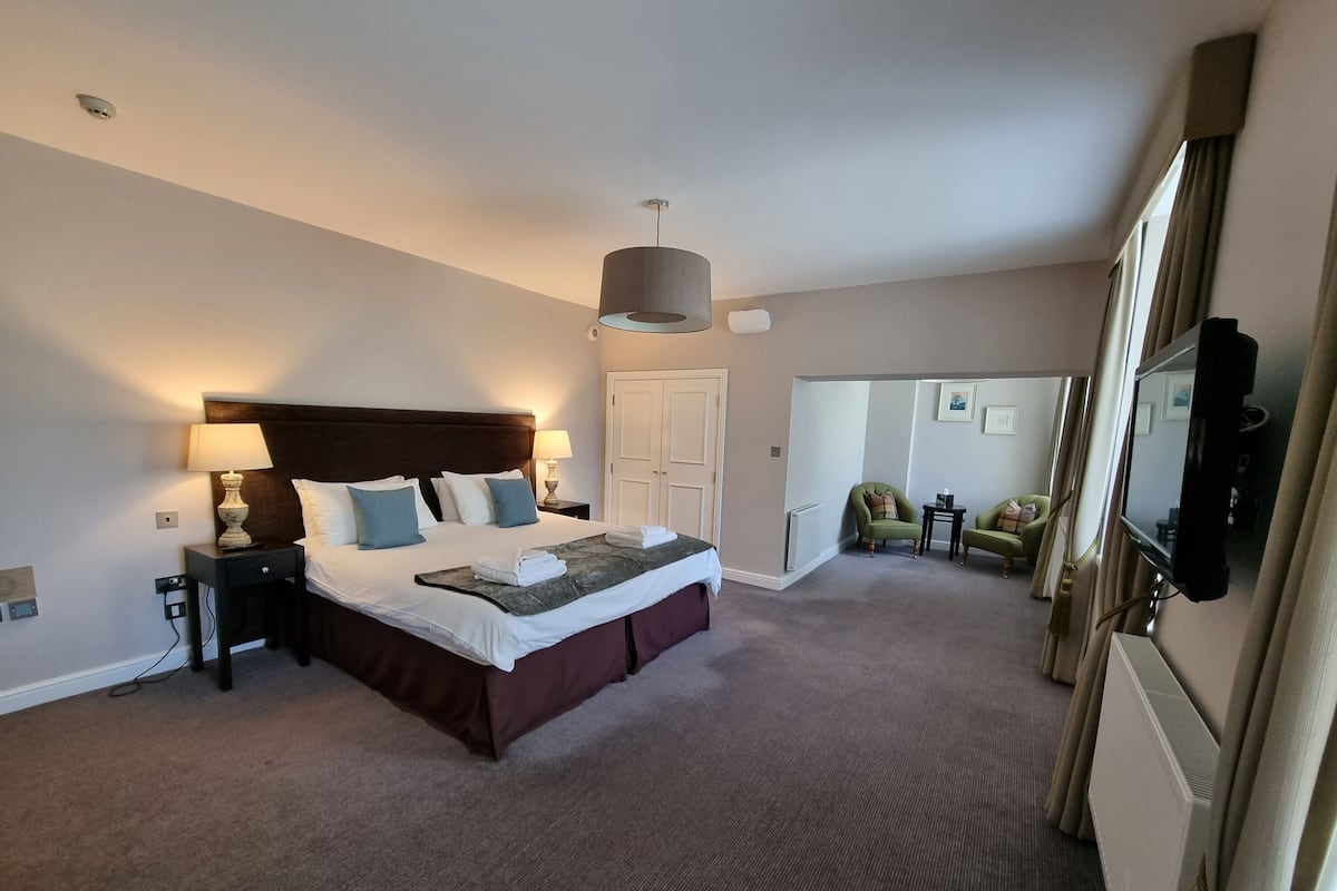 A hotel room with a large bed, bedside tables, a lamp, a mirror, and a view of a balcony area.