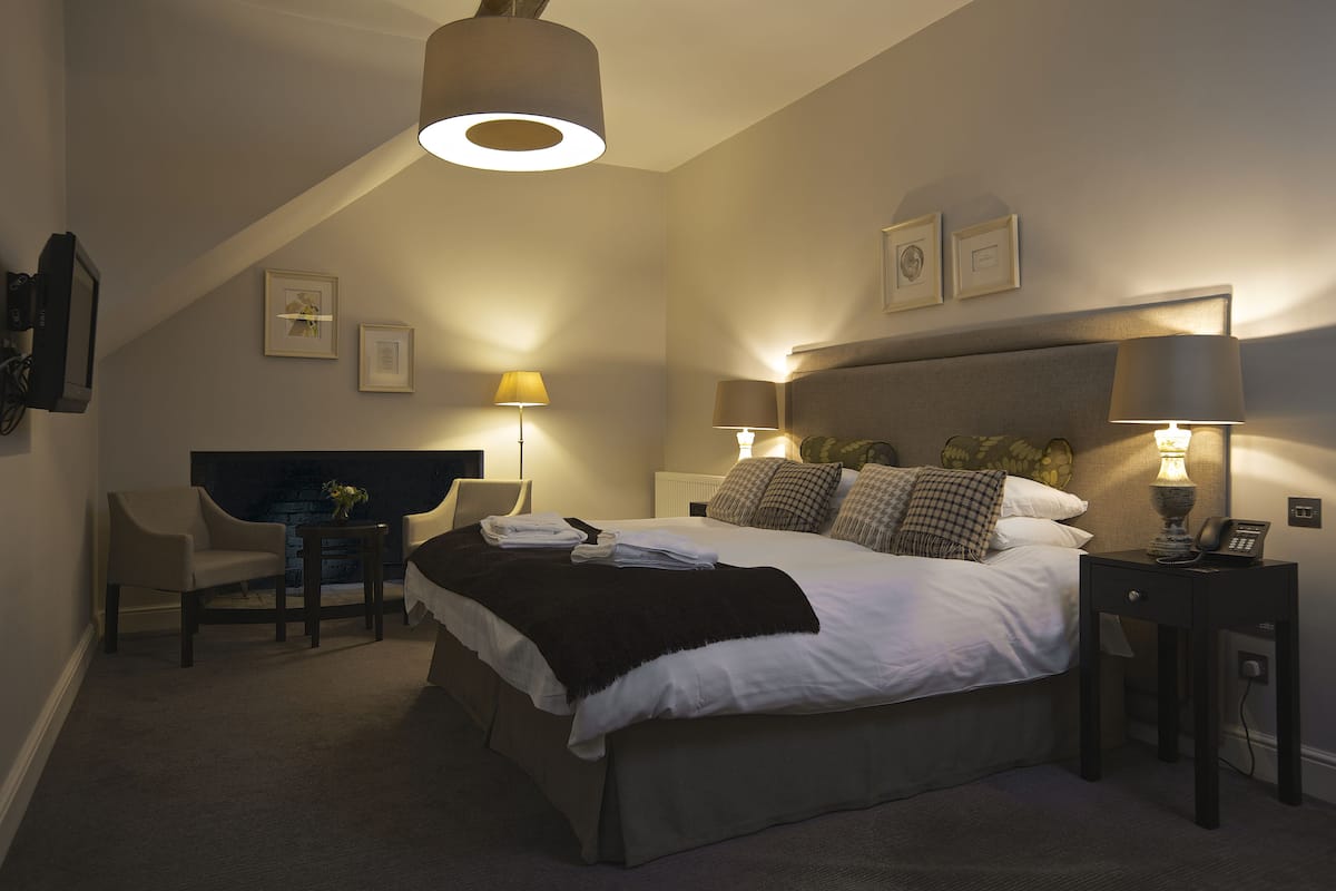 A bedroom with a large bed, two bedside tables with lamps, a chair, and a desk with a lamp.