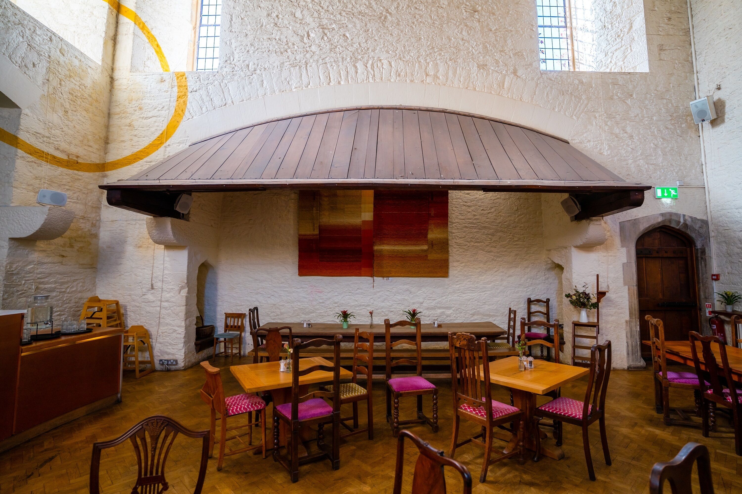 A restaurant with wooden tables and chairs, a stone wall, and a wooden ceiling.