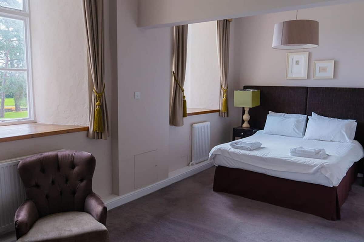 A hotel room with a bed, a chair, a nightstand, a lamp, and a window with curtains.