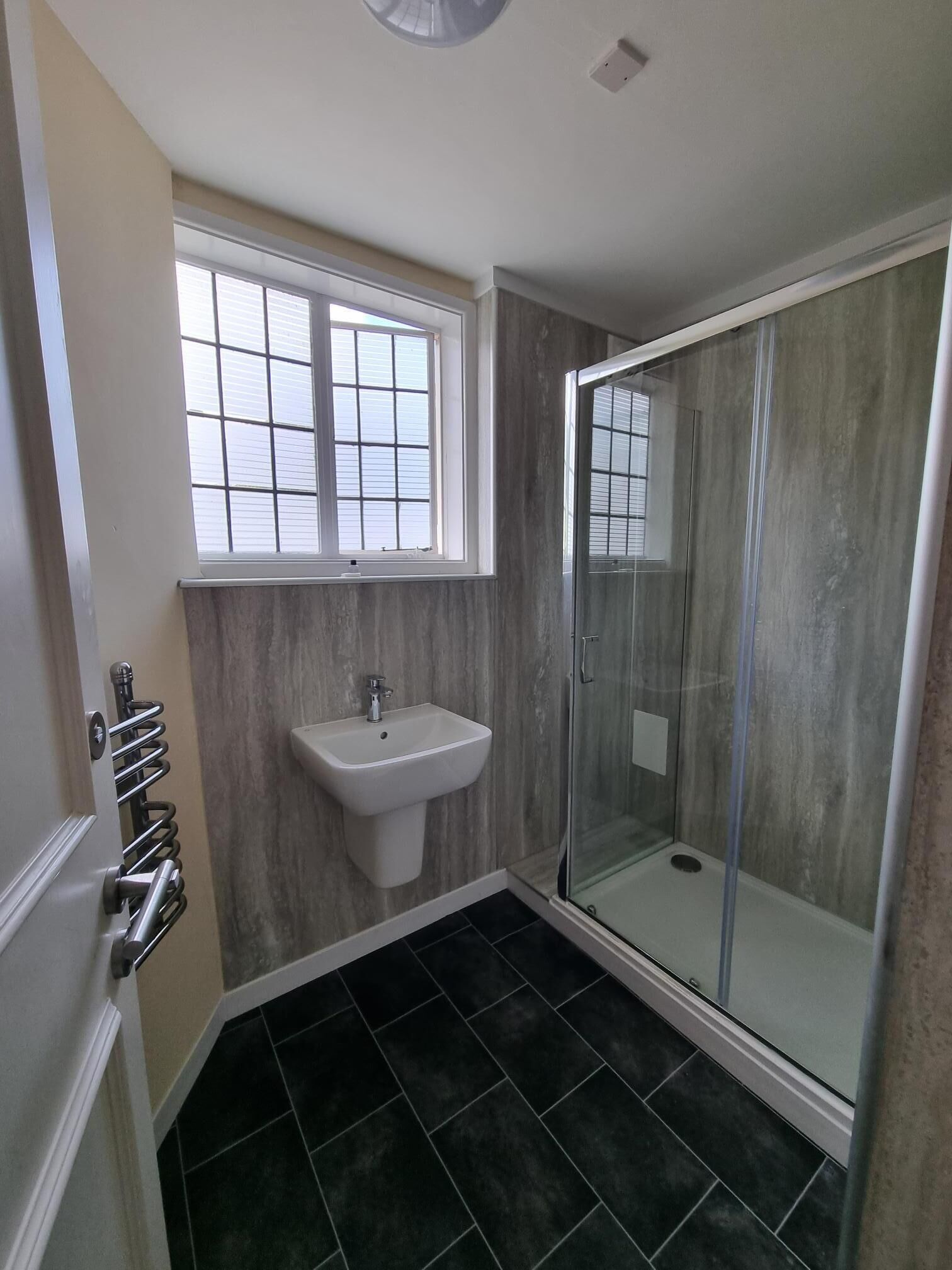 A bathroom with a glass shower enclosure, a sink, and a window.