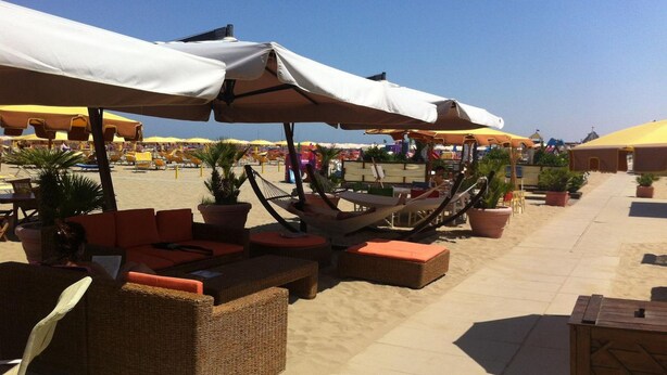 A beachside lounge area with wicker furniture, potted plants, and umbrellas providing shade. - Hotel Staccoli (Rimini)