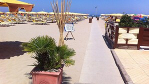 A beachside hotel with rows of sun loungers and umbrellas, a pathway leading to the beach, and a signboard. - Hotel Staccoli (Rimini)