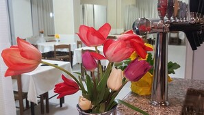 A dining area with a table set for two, a vase of tulips, and a bar with taps. - Hotel Staccoli (Rimini)