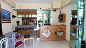 A hotel lobby with a reception desk, seating area, and a kitchen in the background. - Hotel Staccoli (Rimini)