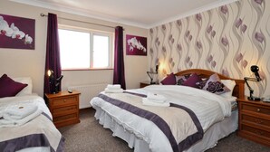 A hotel room with two beds, a window with curtains, a radiator, and artwork on the walls. - Atlantic View (Galway)