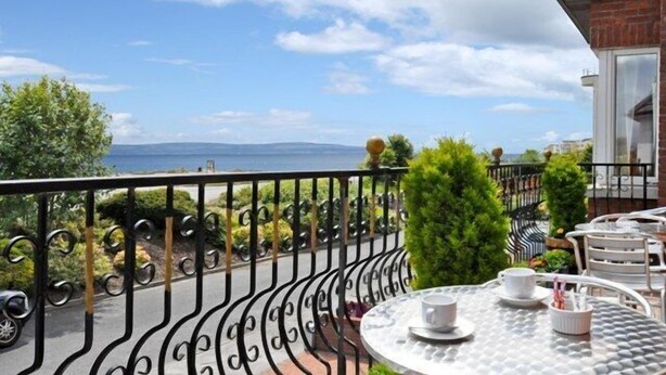A balcony with a view of the sea, a table with cups, and a building with a brick facade. - Atlantic View (Galway)