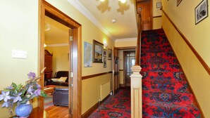 A hallway with a red carpeted staircase, wooden doors, and a dining area with a vase of flowers. - Atlantic View (Galway)