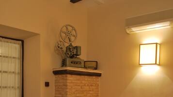A living room with a brick fireplace, a beige sofa, red chairs, a small round table, and a flat-screen TV.