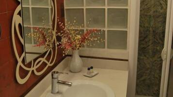 A bathroom with a white sink, a mirror with a decorative frame, a vase with flowers, and a frosted glass window.