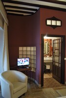 Una habitación con televisión, una silla, un espejo y una puerta que da a un baño.