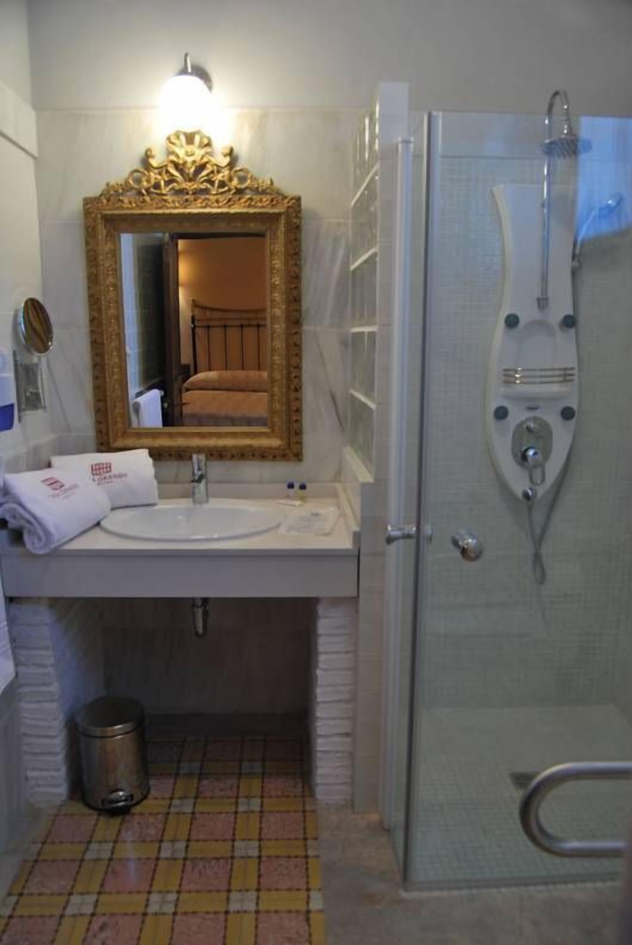 A bathroom with a white sink, a mirror with a gold frame, and a shower enclosure.